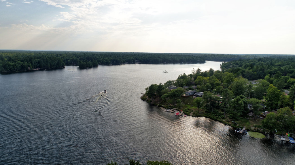 Sunset aerial view of Lantern Bay Resort in Muskoka featuring a boat driving down the river. 