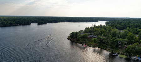 Sunset aerial view of Lantern Bay Resort in Muskoka featuring a boat driving down the river.